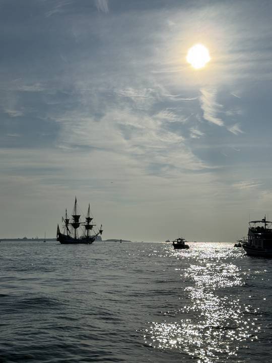 A tall ship anchored in the glare on a summer evening