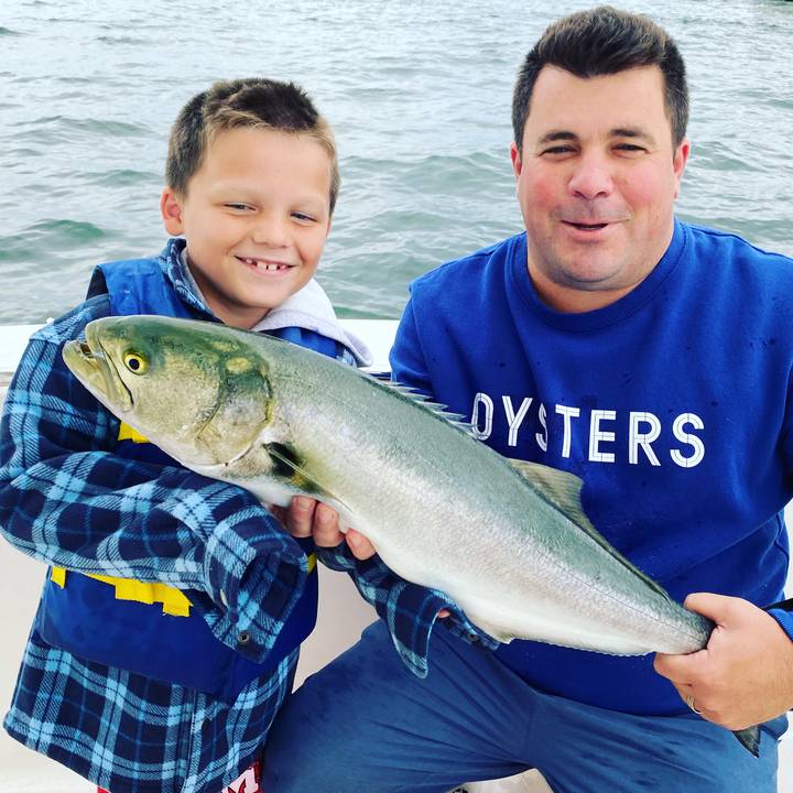 A bluefish held between two anglers on the boat