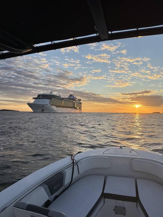 A cruise ship heading out under a broken sunset sky