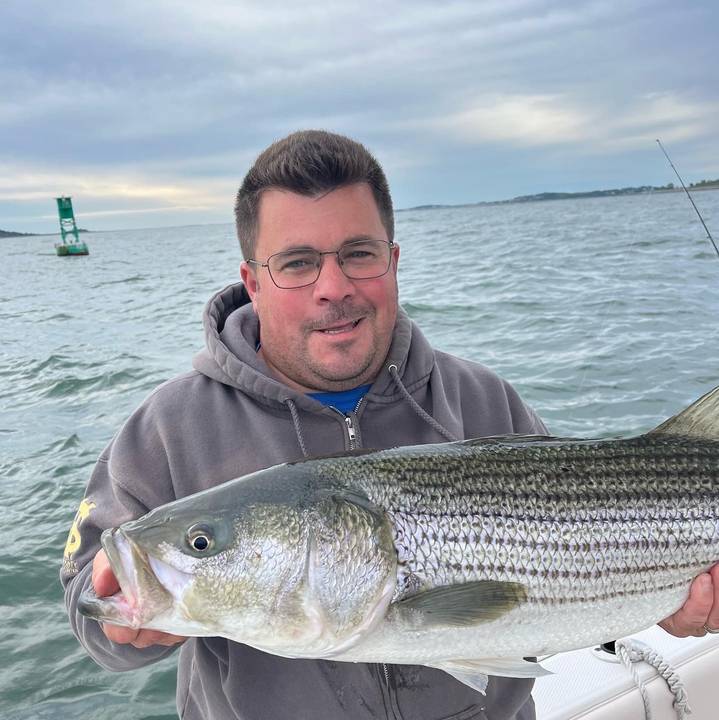Striper held up beside a channel buoy at dusk