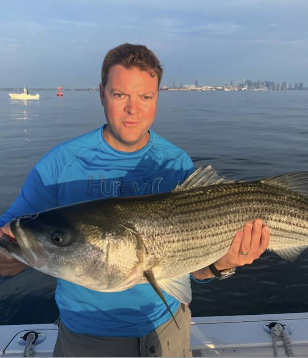 Striper held up at sunrise with the Boston skyline behind