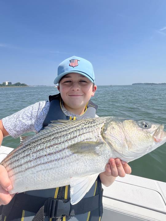 A young angler in a ball cap holding up a striped bass