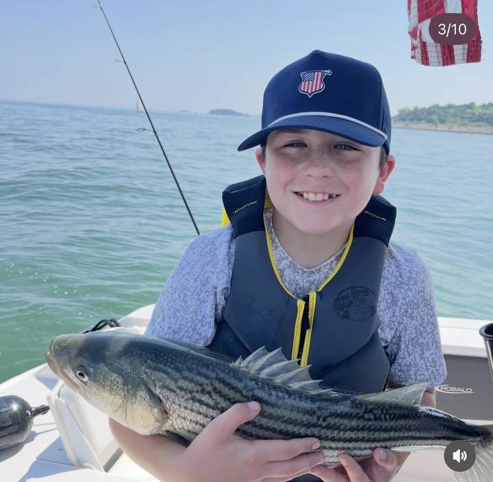 A young angler in a flag cap holding a striped bass