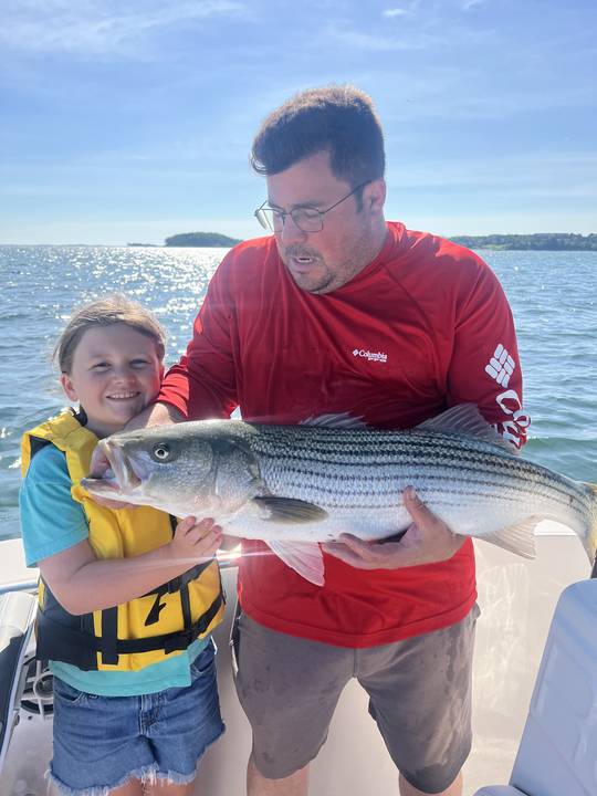 A young angler and a striped bass held together on the bow