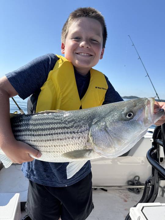A young angler holding a striped bass in a life jacket